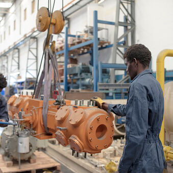 Two afro-american workers are using an industrial crane and a adjustable wrench at a factory
