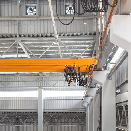 Overhead crane and hook on steel beam with factory wall background.
