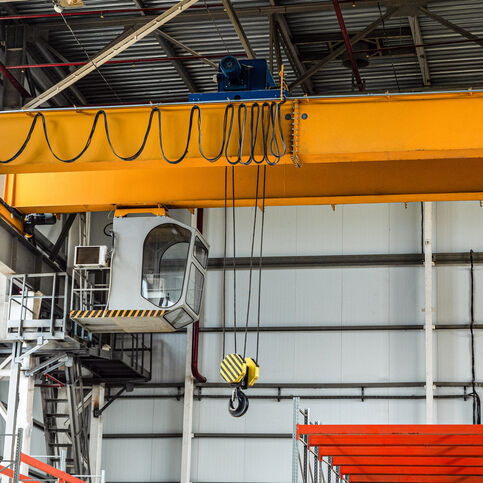 Overhead crane with hook in engineering plant shop. Cabin of crane operator with jib crab trolley. Landing staircase.